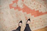 Distressed vintage Oushak carpet displaying a burnt orange stepped medallion outline and patterned ivory field.