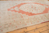 Distressed Oushak rug corner featuring burnt orange medallion outline and muted floral field.