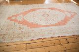 Distressed vintage Oushak carpet with large burnt orange medallion and soft ivory tones.
