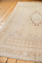 Muted ivory and beige distressed Oushak rug corner with geometric border and worn pile.