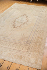 Distressed Oushak corner with faded beige borders and faint planted floral spandrel.