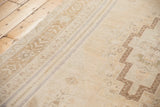 Vintage distressed Oushak rug shows geometric border and muted field motifs in ivory, beige, and soft blue.