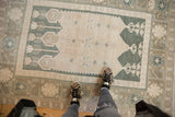 Faded green blossom motifs on the ivory field of a vintage distressed Oushak rug.