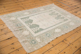 Distressed vintage Oushak rug, angled view, ivory field, powder blue medallion, and floral-banded border.