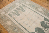 Distressed Oushak rug corner with ivory field, powder blue serrated medallion, and patterned border.