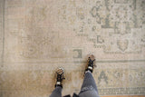 Distressed Oushak rug with geometric motifs, low pile, and speckles of foundation showing.
