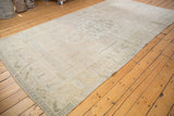 Distressed Oushak rug corner, showing low pile wear and faded seafoam green motifs.