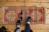 Distressed Oushak rug detail: geometric medallion with primitive florals in raspberry red and navy.
