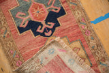 Distressed Oushak rug corner with fringe, low pile, and raspberry geometric design.