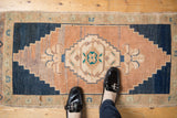Foot on a distressed vintage Turkish Oushak rug, showing its abrashed peach-toned field.
