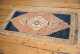 Vintage distressed Oushak rug corner with stepped navy border, floral motifs, and fringe.
