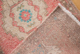 Distressed Oushak rug corner shows soft blush pile, woven reverse, intact side cord, and fringe.