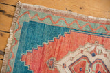 Distressed Oushak rug corner with fringe, brick red and turquoise geometric patterns.