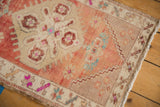Distressed Oushak rug corner showing faded blush, beige, blue floral patterns and white fringe.