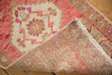 Distressed Oushak rug corner showing worn ivory pile, pink motifs, woven foundation, and selvage.