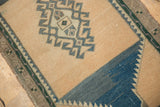 Distressed Oushak rug corner showing sand field, dusty navy, and forest green geometric border.