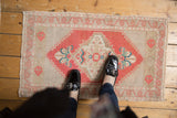 Distressed vintage Oushak rug mat with brick red medallion, ivory field, and floral finial.