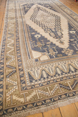 Distressed vintage Oushak rug corner featuring dusty navy blue, beige serrated leaf border.