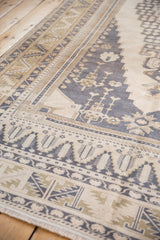Distressed Oushak rug corner, dusty navy blue spandrel, and serrated leaf border.