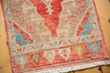 Distressed Oushak rug corner with worn pile, muted cherry red border, and ivory fringe.