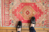 Distressed hand-knotted Oushak rug showing fringe and geometric border in cherry red and dusty gold tones.
