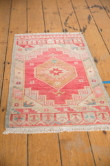 Distressed Oushak rug corner with time-softened cherry red field, geometric ivory border, and fringe.