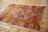 Distressed vintage Oushak rug corner showing textured pile with saffron, pink, and aubergine hues.