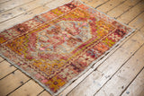 Distressed vintage Oushak rug corner showing faded pink, gold, and aubergine patterns.