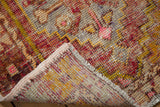 Distressed vintage Oushak rug detail, showing time-softened pile with aubergine, saffron, and pink tones, and faint foundation.