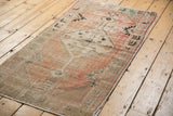 Angled view of distressed vintage Oushak runner with faded blush, ivory, and charcoal patterns.