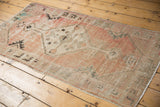 Distressed vintage Oushak rug corner showing faded blush, ivory, and light blue geometric patterns.