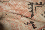 Hand knotted Oushak rug's distressed pile featuring blush rose and charcoal geometric motifs.