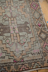 Distressed Oushak runner pile, showing geometric patterns in faded apricot, gray, and blush pink.