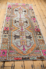 Corner of distressed Oushak runner, showing mostly even wear, pink, orange, brown geometric motifs.
