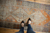 Distressed Oushak runner pile with vivid tangerine and muted blue geometric patterns.