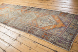 Distressed Oushak rug runner's end showcasing faded gray, aubergine, and tangerine border motifs.