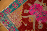 Distressed vintage Oushak rug corner showing aqua border, bold pink motifs, and vibrant red field.