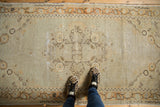 Distressed ivory and tangerine Oushak runner, showing faded medallion, textural wear, and a person's feet.