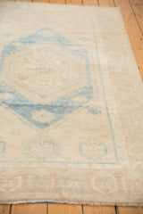 Distressed Oushak rug end, showing low pile, faded aqua geometric border, and beige hues.