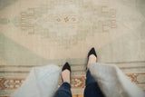 Distressed vintage Oushak carpet showing low pile texture and faded geometric end motifs.
