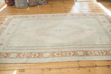 Distressed Oushak rug with terra cotta geometric border and pale silver field motifs.