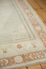 Distressed Oushak rug corner with terra cotta geometric border and low beige pile.