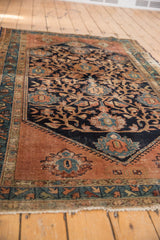 Malayer rug's lower right corner with dark blush copper field, geometric border, and tattered fringe.