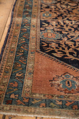 Vintage Malayer rug corner with wear, intricate navy vinery, dark blush field, and geometric border.