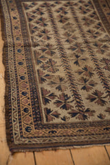 Antique Belouch rug detail: hand-knotted tribal motifs, beige field, dark blue border, and frayed edge.