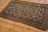 Tattered end and intricate borders of an antique Belouch rug, showing chocolate brown and navy starburst motifs.