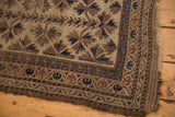 Antique hand knotted Belouch rug corner: chocolate brown starburst motif, worn pile, tattered overcast edge.