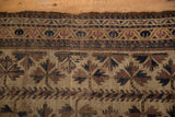 Antique Belouch rug detail: worn pile, tattered end, starburst floral motif in brown, navy, beige.