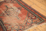 Worn vintage Hamadan rug with exposed foundation, red field, navy pawn border, and tattered fringe.