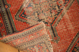 Folded vintage Hamadan rug corner, revealing wear, exposed foundation, and red, blue pawn border.